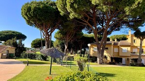 A well-maintained garden with mature trees, a thatched umbrella, and a paved walkway. - ✨ Luminous townhouse overlooking the Golf on the beach of Novo Sancti Petri (Chiclana de la Frontera)