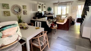 A spacious living area with a dining table, chairs, and a sofa. There is a kitchen area with cabinets and a clock on the wall. - ✨ Luminous townhouse overlooking the Golf on the beach of Novo Sancti Petri (Chiclana de la Frontera)
