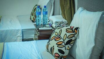 Habitación de hotel con cama, almohadas, mesita de noche, control remoto y agua embotellada.