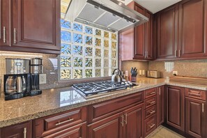 Una cocina con estufa a gas, cafetera y ventana con vistas a árboles.