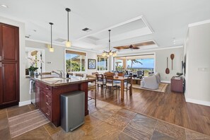 A spacious kitchen with a central island, dining area with chairs, and a view of the outdoors. - Spacious Ocean View condo with AC in Mauna Kea Resort (Waimea)