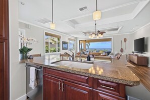 A modern kitchen with a central island, granite countertops, and a large window overlooking a tropical landscape. - Spacious Ocean View condo with AC in Mauna Kea Resort (Waimea)