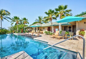 A pool area with lounge chairs and umbrellas, surrounded by palm trees and a building with a tiled roof. - Spacious Ocean View condo with AC in Mauna Kea Resort (Waimea)