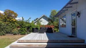 A wooden deck with outdoor furniture, a white building with a door and windows, and a wooden fence.