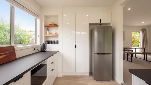 A modern kitchen with white cabinets, a stainless steel refrigerator, and a window providing a view of greenery outside.