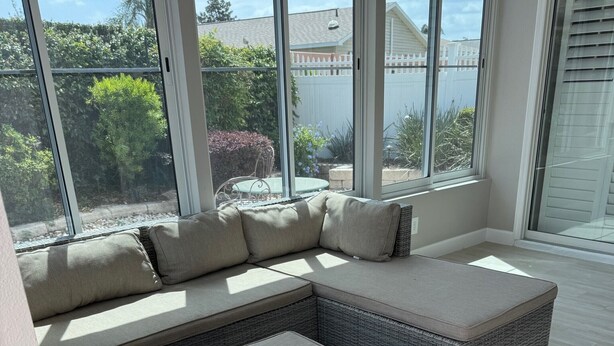 A large sectional sofa with a matching ottoman in a bright room with large windows. - Beautiful Courtyard Villa near Lake Sumter Landing (The Villages)