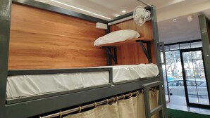 A bunk bed room with a wooden headboard, a ceiling fan, and a view of the street through a large window. - S. G. P Dormitory (Mathura)