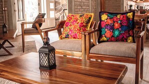 Un fauteuil en bois agrémenté d’un coussin aux motifs floraux colorés, une table basse en bois et une lanterne.