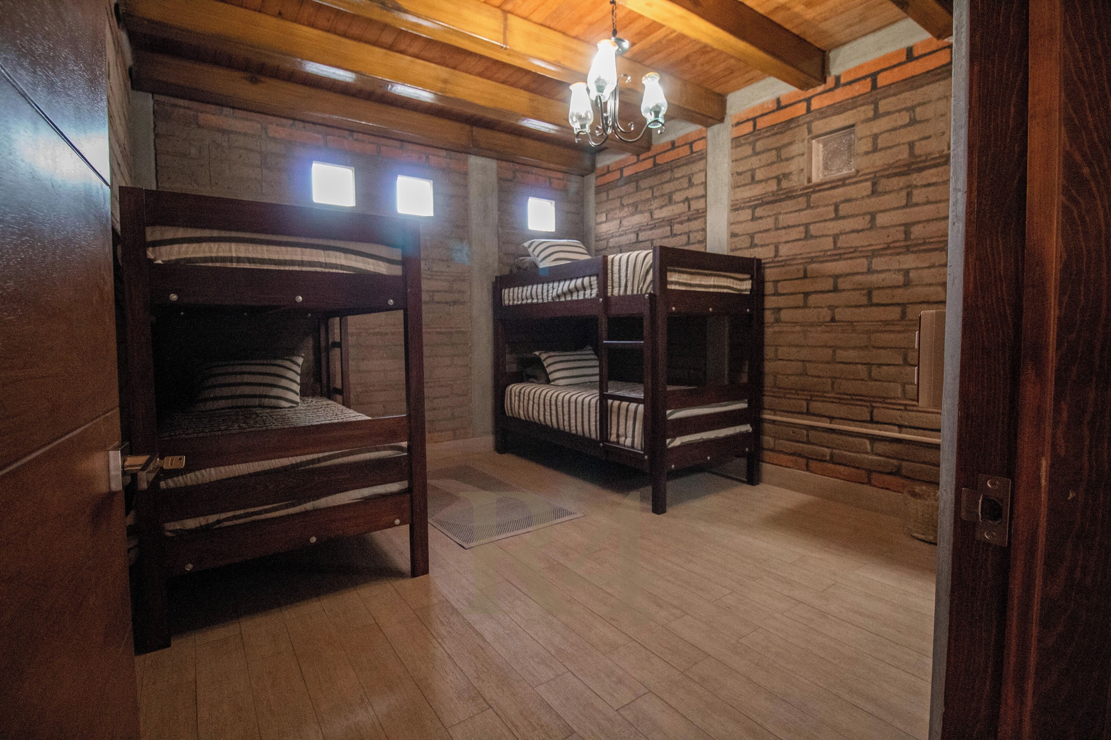 A room with two bunk beds, wooden floors, brick walls, and a chandelier.
