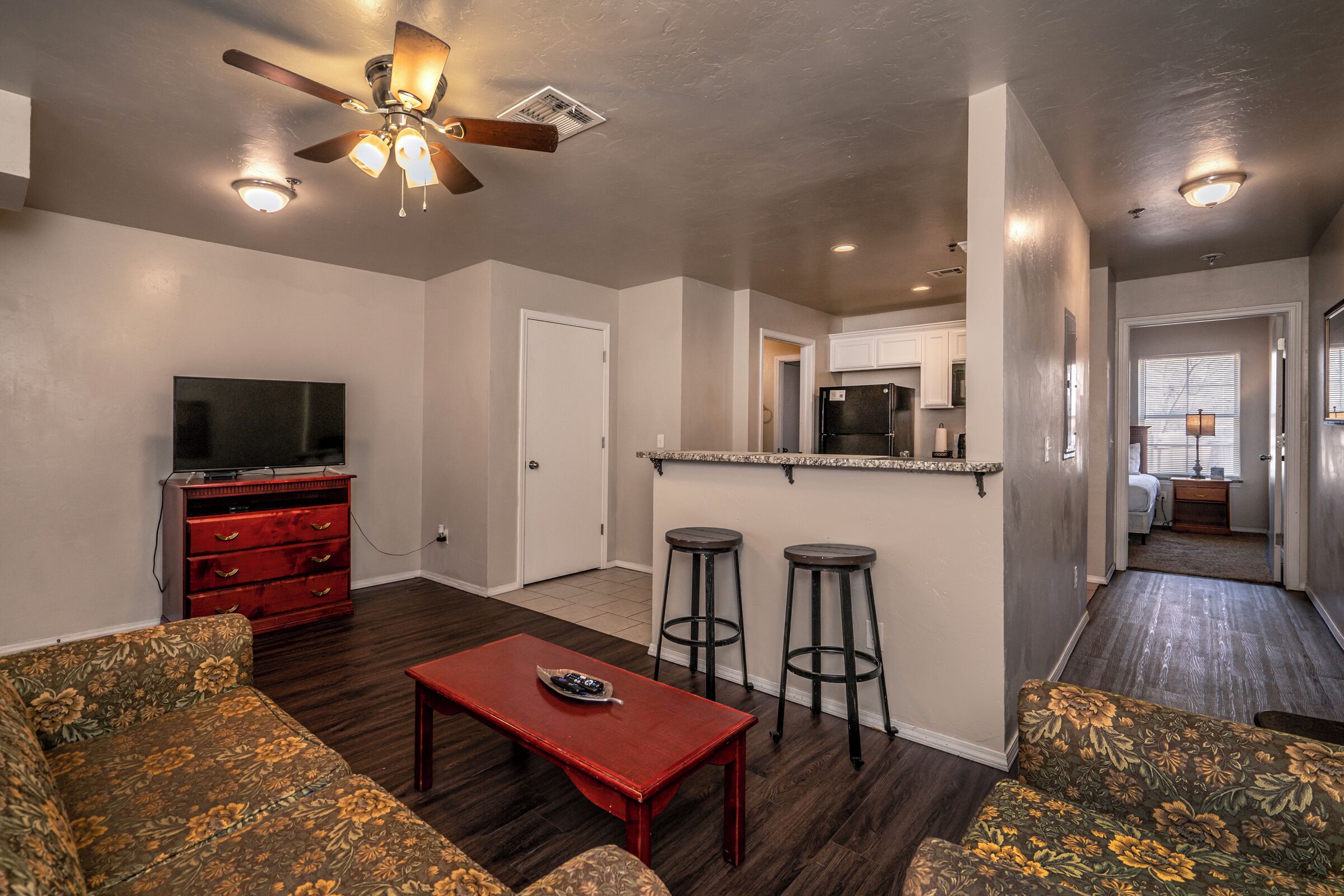 A living room with a red coffee table, two patterned sofas, a TV, and a ceiling fan.
