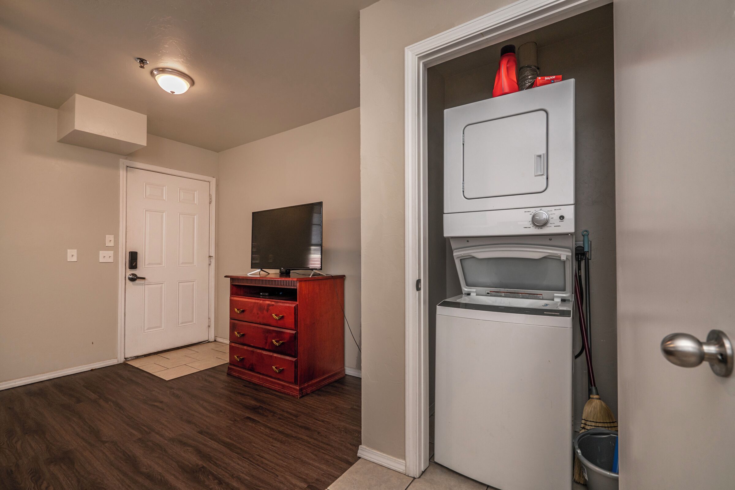 Un couloir avec un plancher en bois, une porte blanche, une commode rouge et un lave-linge.