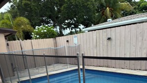 A swimming pool with a metal fence, a tiled deck, and a wooden fence in the background.