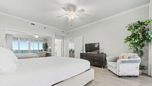 Un dormitorio moderno con una cama grande, ventilador de techo, televisión y vistas al balcón.