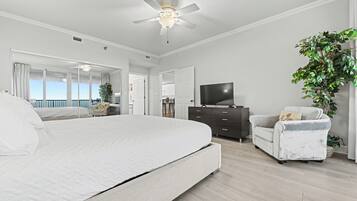 A modern bedroom with a large bed, a ceiling fan, a TV, and a view of the balcony.