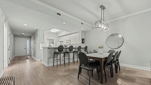 Un comedor moderno con piso de madera, una mesa central con sillas, una lámpara colgante y un espejo redondo en la pared.