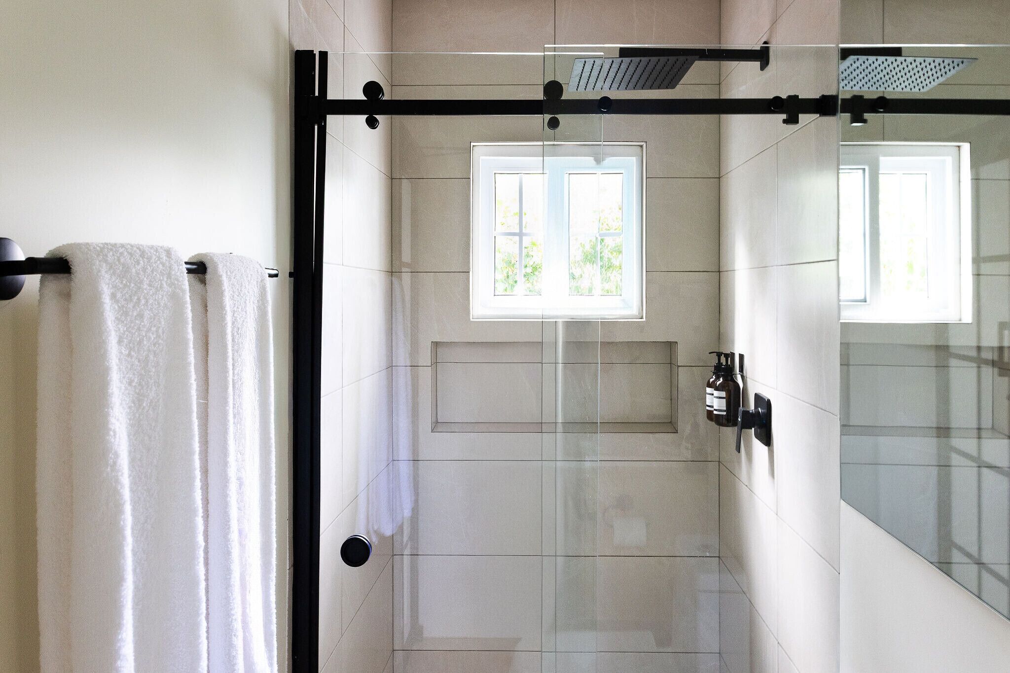 A modern bathroom with a glass shower enclosure, a window providing natural light, and a towel rack.