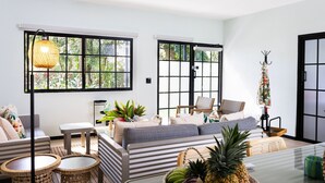 Een moderne woonkamer met een bank, twee bijzettafeltjes, een salontafel en een groot raam met uitzicht op groen.
