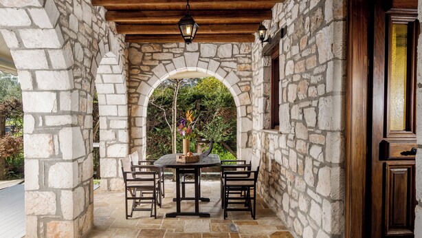A stone archway leading to a patio with a table and chairs, a wooden door, and a hanging lantern. - Grantzaos Villas Zante (Agios Sostis)