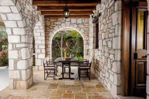 A stone archway leading to a patio with a table and chairs, a wooden door, and a hanging lantern. - Grantzaos Villas Zante (Agios Sostis)