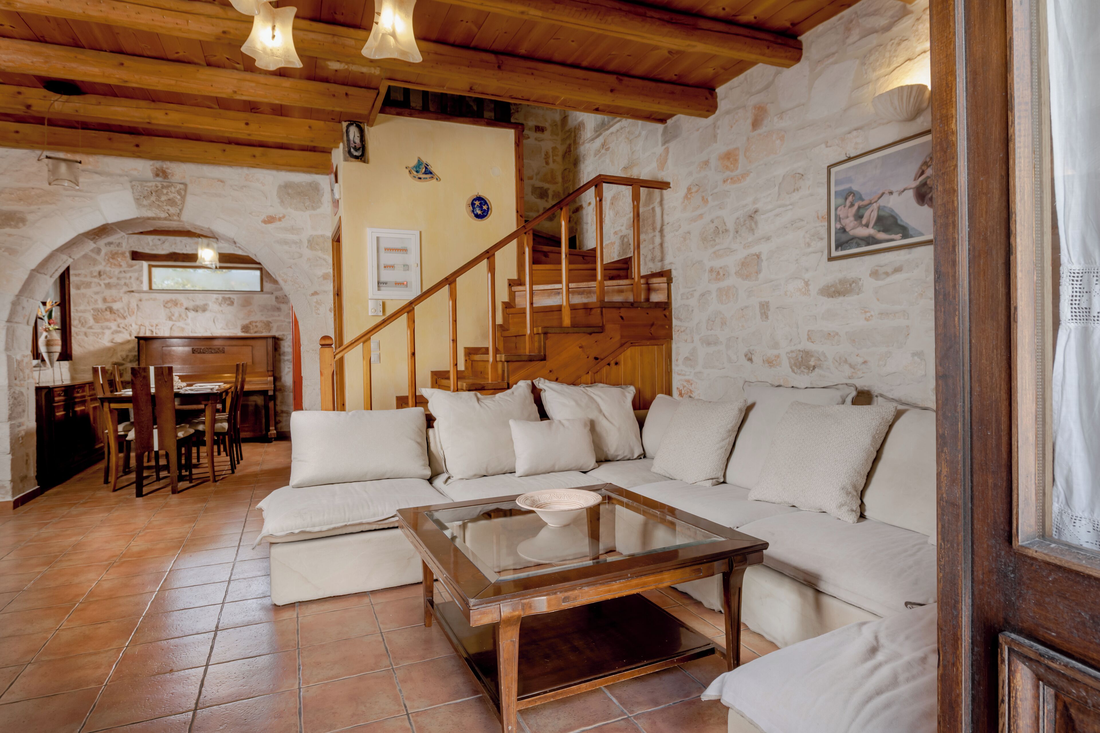 Un saló d'estar acollidor amb una escala de fusta, un sofà i zona de menjador amb taula i cadires.