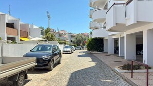 En smal brostensgade med moderne bygninger, en parkeret lastbil og et par biler.