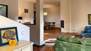 Un salon avec un canapé vert, un coin repas avec une table et des chaises, une cheminée et un escalier menant à un autre niveau.