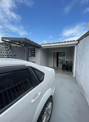 A white car parked in a covered driveway with a patio area and a brick wall. - House in Florianópolis (Florianópolis)