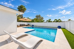Una piscina con un deck blanco, sillas de descanso y una valla blanca.