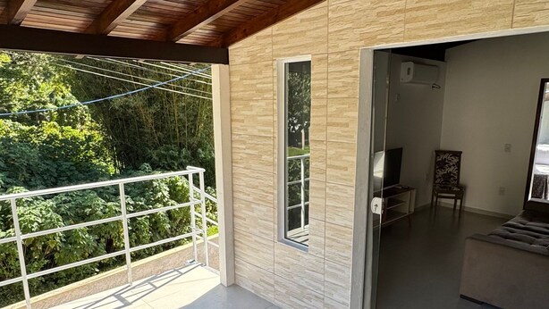 Un patio cubierto con mobiliario de mimbre, vista a follaje y un interior moderno con televisor y asientos.