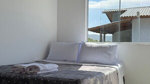 Un dormitorio con cama, almohadas, una ventana y vista a un edificio.