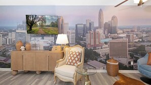 Een kamer met een stadsgezicht muurschildering, een houten kast met decoratieve objecten, een stoel, een tafel met een lamp en een plafondventilator.
