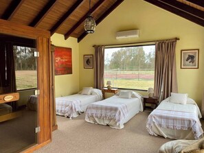A room with three beds, a wooden ceiling, a large window with curtains, and a view of a sports field. - Gorgeous 7-bedroom farmhouse with AC in charming Soca (Departamento de Canelones)