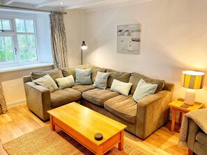 Un salon chaleureux avec un canapé d’angle, une table basse en bois et une lampe sur une table d’appoint.