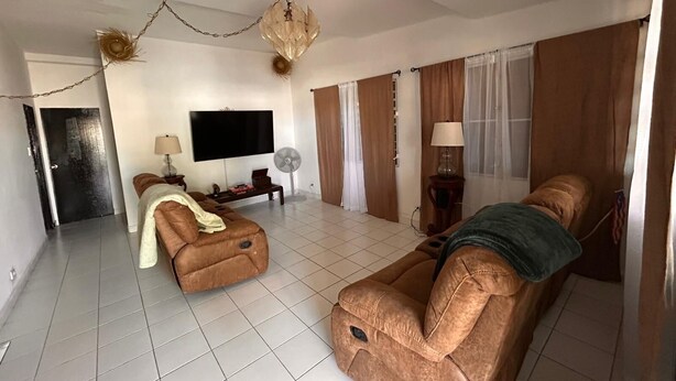 A spacious living room with a large flat-screen TV, two sofas, a chandelier, and a fan. - Cozy 3-bedroom house in serene Carolina with AC (Carolina)