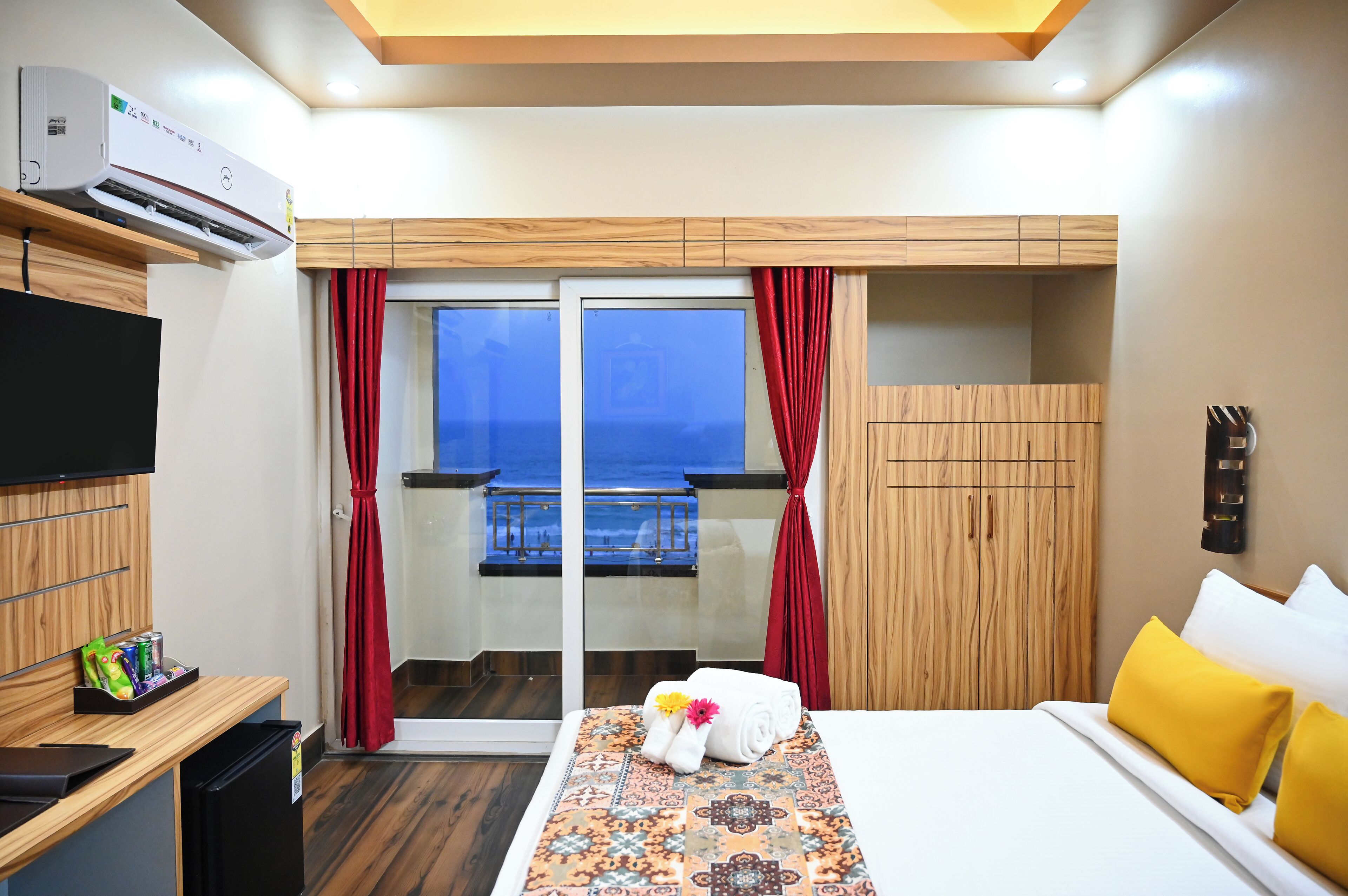 A hotel room with a bed, a TV, a desk, a minibar, a balcony with a view, and a wooden wardrobe.