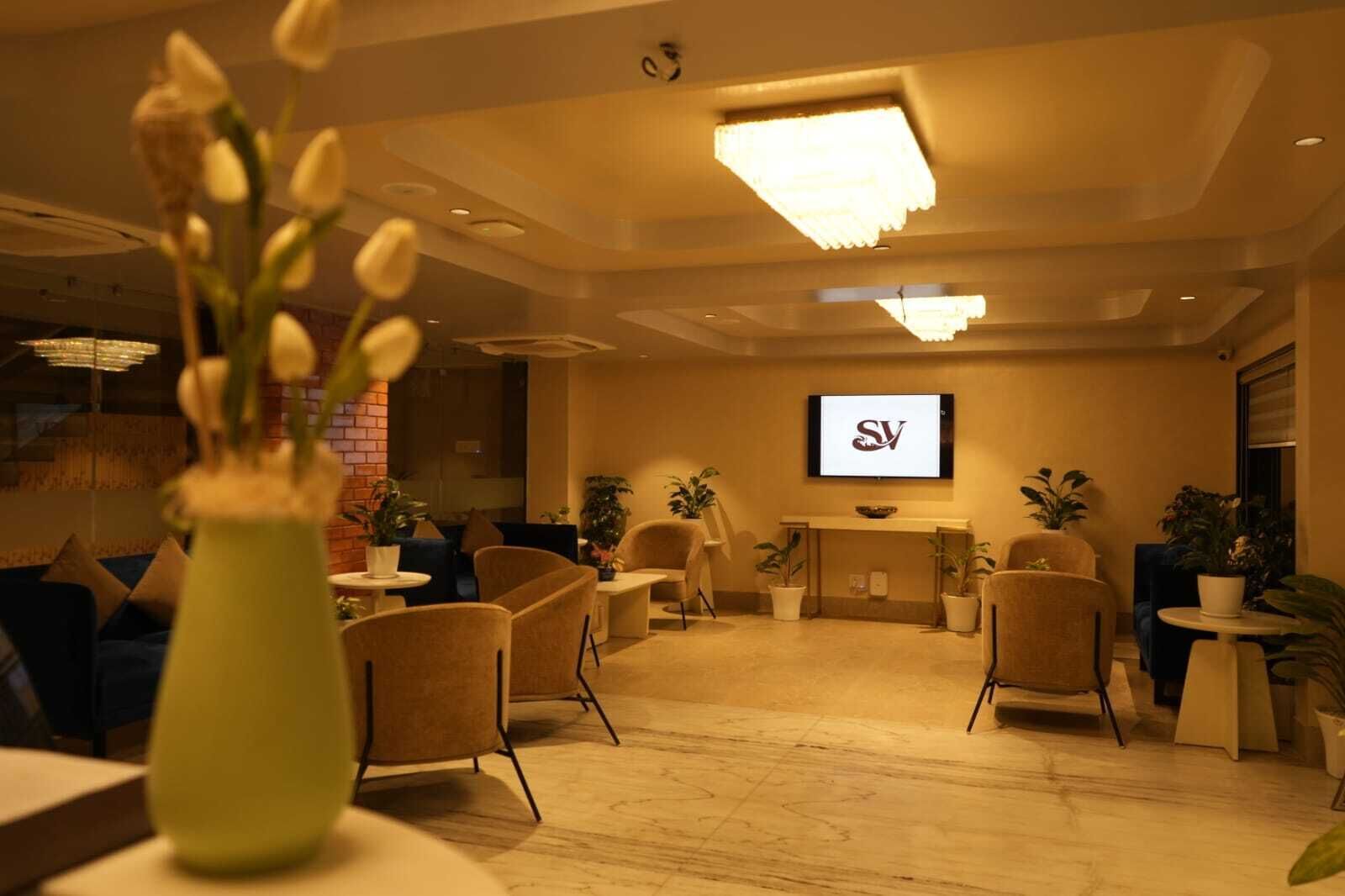 A modern lounge area with comfortable seating, a reception desk, and a television screen displaying a logo.