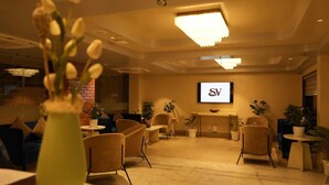 A modern lounge area with comfortable seating, a reception desk, and a television screen displaying a logo. - The Sea Valley Beach front Hotel (Puri)