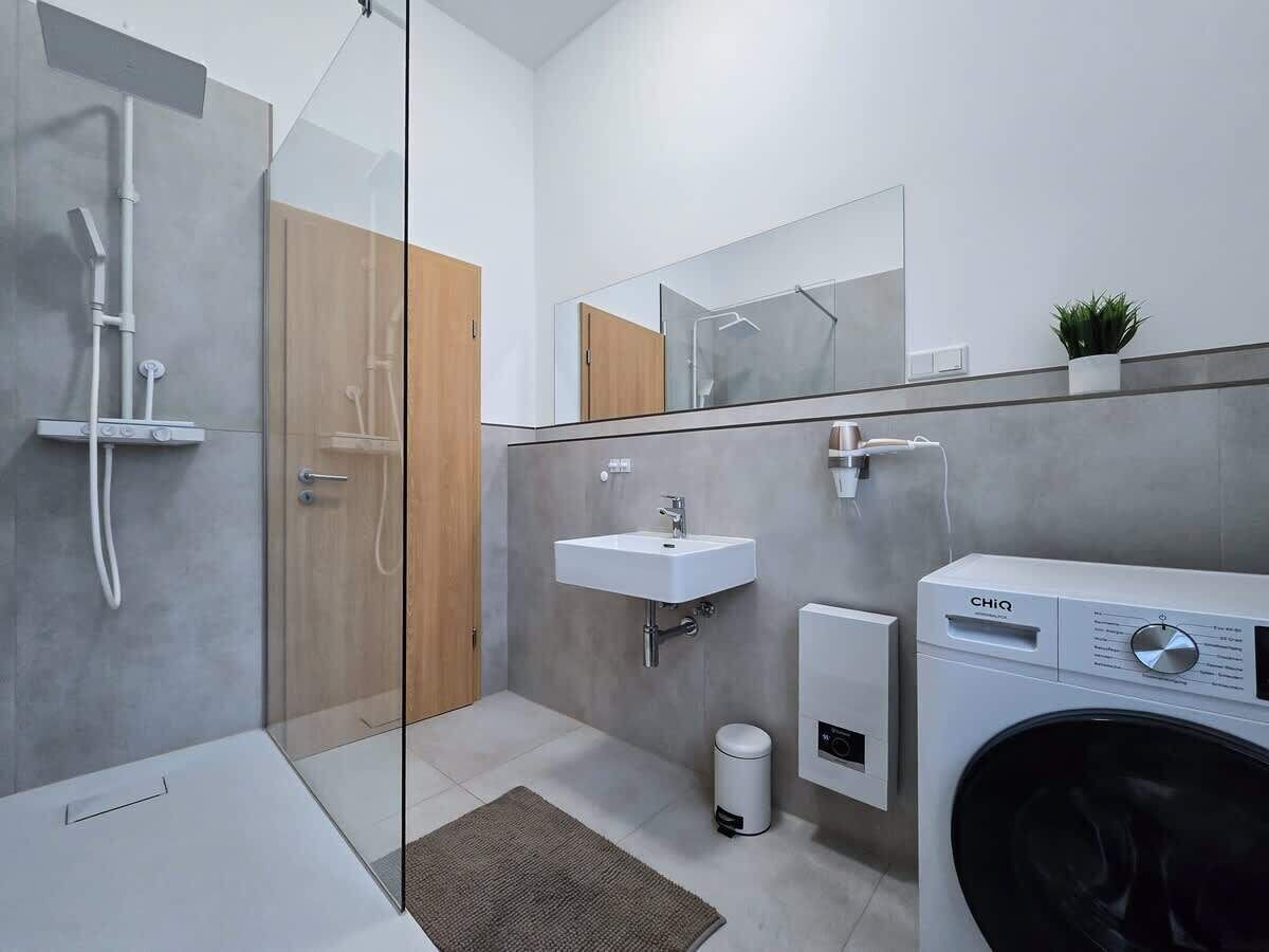 Ein modernes Badezimmer mit Duschkabine aus Glas, einem Waschbecken, einem Spiegel und einer Waschmaschine.