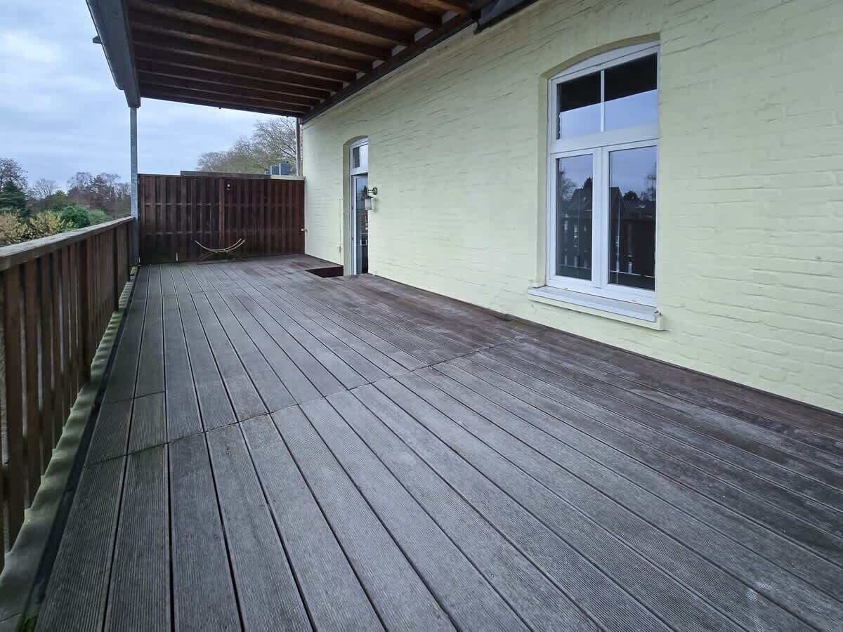 Eine Holzdielen-Terrasse mit Geländer, einem Fenster und einer Tür an einem Gebäude.