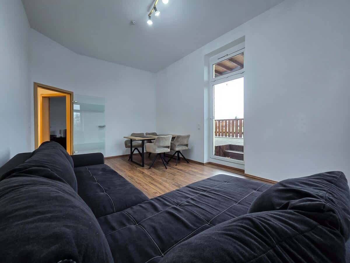 Ein modernes Zimmer mit einer schwarzen Couch, einem Esstisch mit Stühlen und einem großen Fenster mit Blick.