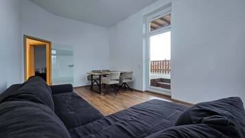 Ein modernes Zimmer mit einer schwarzen Couch, einem Esstisch mit Stühlen und einem großen Fenster mit Blick.
