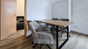 A room with a wooden floor, a wooden table with chairs, a whiteboard, and a wardrobe. - Alpha Apartments: 2BR for 4, Quiet Retreat (Krefeld)