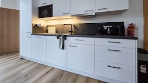 A modern kitchen with white cabinetry, a black countertop, a built-in microwave, and a coffee maker. - Alpha Apartments: 2BR for 4, Quiet Retreat (Krefeld)