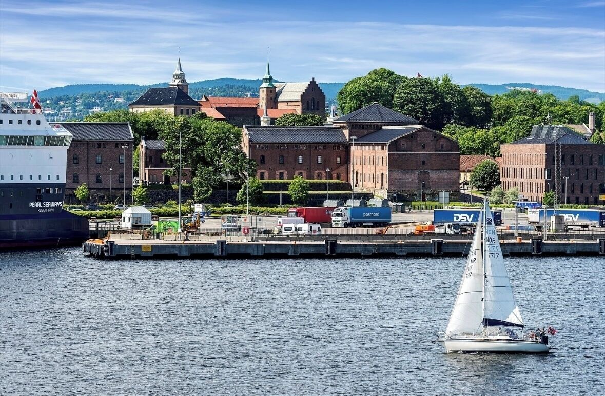 A harbor with a sailboat, a large ship, and historic buildings in the background.