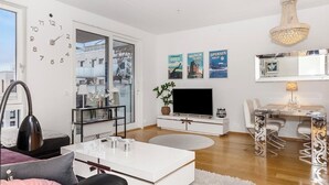 Un salon moderne doté d’un grand téléviseur à écran plat, d’un coin repas agrémenté d’un lustre et d’une horloge murale.
