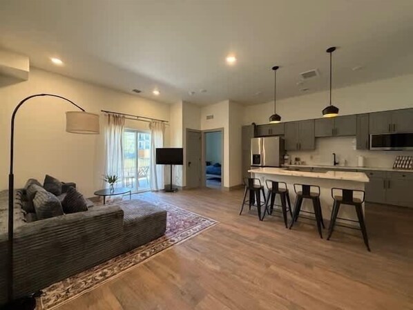 A modern living room with a sofa, a flat-screen TV, and a dining area with bar stools.