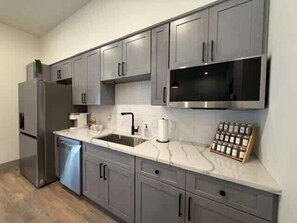 A modern kitchen with grey cabinets, stainless steel appliances, a marble countertop, and a built-in microwave.