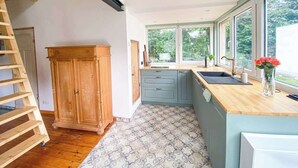 A kitchen with a wooden cabinet, a wooden countertop, and a window with a view of greenery. - Tiny house in Rangsdorf for 4 people + fireplace (Rangsdorf)