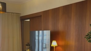 A modern living room with a wooden herringbone floor, a large flat-screen TV, a comfortable armchair, a small round coffee table, and a lamp. - 4-bedroom penthouse with spectacular sea views (Thessaloniki)