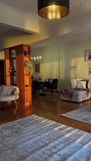 Una sala de estar moderna con un separador de madera, un comedor con mesa y sillas, y una lámpara de araña grande.